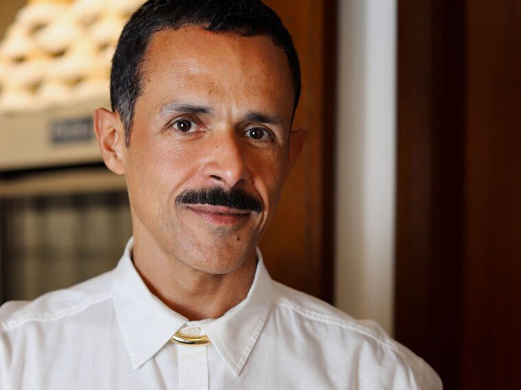 Retrato de homem de camisa branca e bigode em ambiente interno.