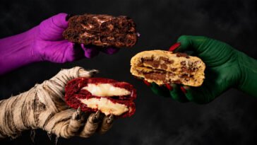 Três cookies recheados, de massas vermelha, clara e chocolate, segurados por mãos fantasiadas de múmia e pintadas de roxo e verde.