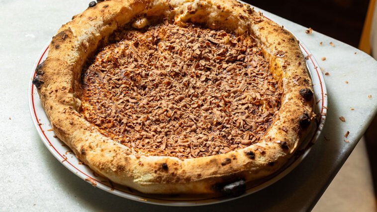 Pizza doce com borda alta e dourada, recheio cremoso e cobertura de raspas de chocolate.