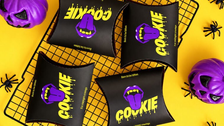Embalagens pretas com a palavra Cookie em amarelo e boca roxa, cercadas por abóboras roxas e aranhas decorativas.