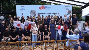 Grupo de participantes posa diante de painel do Rio Coffee Nation, com algumas pessoas segurando placas e certificados.