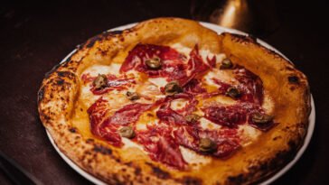 Pizza de borda alta e tostada, coberta com queijo derretido, fatias finas de carne curada e pequenos peda&ccedil;os de cogumelos.