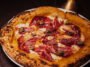 Pizza de borda alta e tostada, coberta com queijo derretido, fatias finas de carne curada e pequenos peda&ccedil;os de cogumelos.